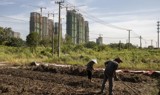 Farmers tend to vegetable plot near high-rise apartment buildings at China Evergrande Group's under-construction Riverside Palace development in Taicang, Jiangsu province, China, on Friday, Sept. 24, 2021. China's housing regulator has stepped up oversight of China Evergrande Group's bank accounts to ensure funds are used to complete housing projects and not diverted to pay creditors.