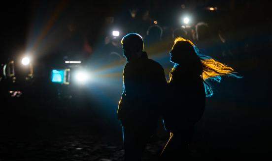2 people in the shadows , with blue and yellow lights shining in the background, imitating the Ukrainian flag