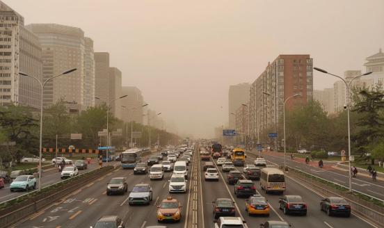 a picture of a big road, with a lot of cars and buildings around, the fog or smog is over the city