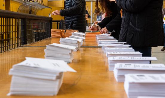 a picture of a table with numerous ballot sheets on it, and people counting votes
