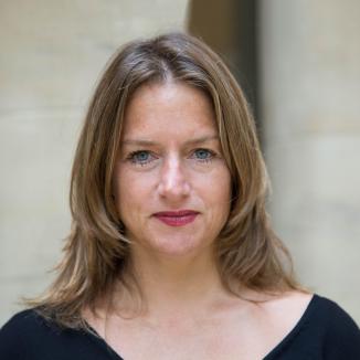 A head-shot of a woman with light brown shoulder length hair. She has blue eyes and wears red lipstick. 