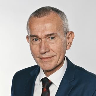 A man with grey hair and in a dark-blue suit smiling at the camera