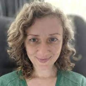 a woman with short curly hair and in a green jumper smiling at the camera