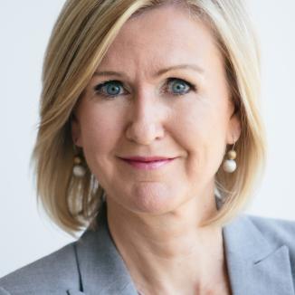 a portrait of a woman with short blonde hair, in a grey suit jacket looking at the camera