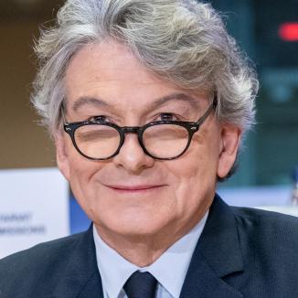 a man with grey hair , in glasses and in a black suit with white shirt and black tie