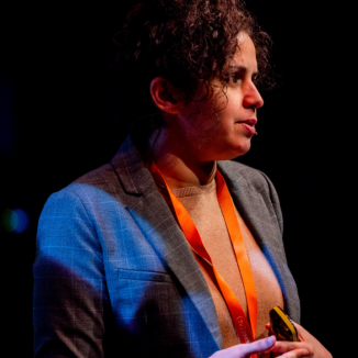 a woman with curly brown hair styled in a high bun, giving a lecture