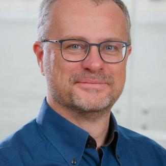 a man with short hair, glasses , wearing a dark blue shirt