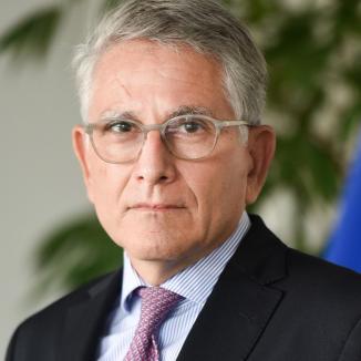 a man with grey hair, in glasses, in a black suit with a pink tie 